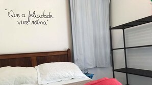Un lit bien fait, avec du linge de lit blanc et rouge, une serviette rouge et une petite étagère contenant des articles de toilette.