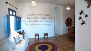 Un salon avec un canapé blanc, un tapis coloré et un mur orné d’une citation en portugais.