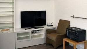 En moderne stue med et fladskærms-tv, et lille bord med en brødrister, en fletstol og indbyggede hylder.