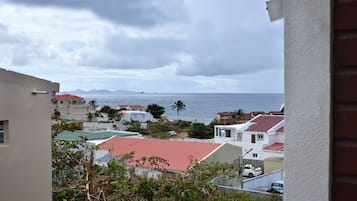 A coastal residential area with houses, a red-roofed building, and a view of the sea and mountains in the distance.