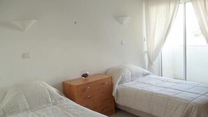 Una habitació amb dos llits, un armari de fusta i una finestra amb cortines.