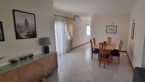 Una zona de menjador amb taula i caires, un sofà, un armari amb objectes decoratius i un quadre amb marc a la paret.