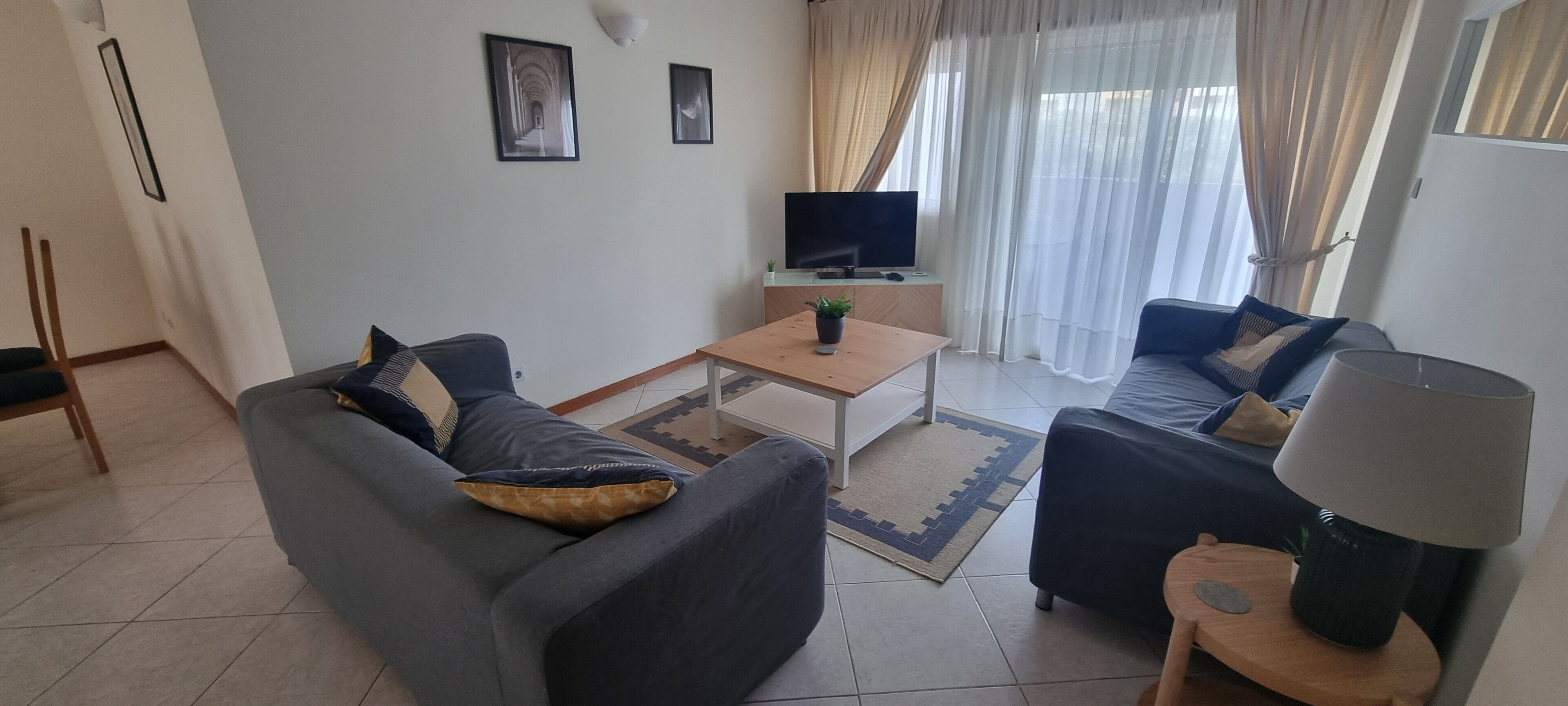 A living room with a sofa, armchair, coffee table, TV, and curtains.