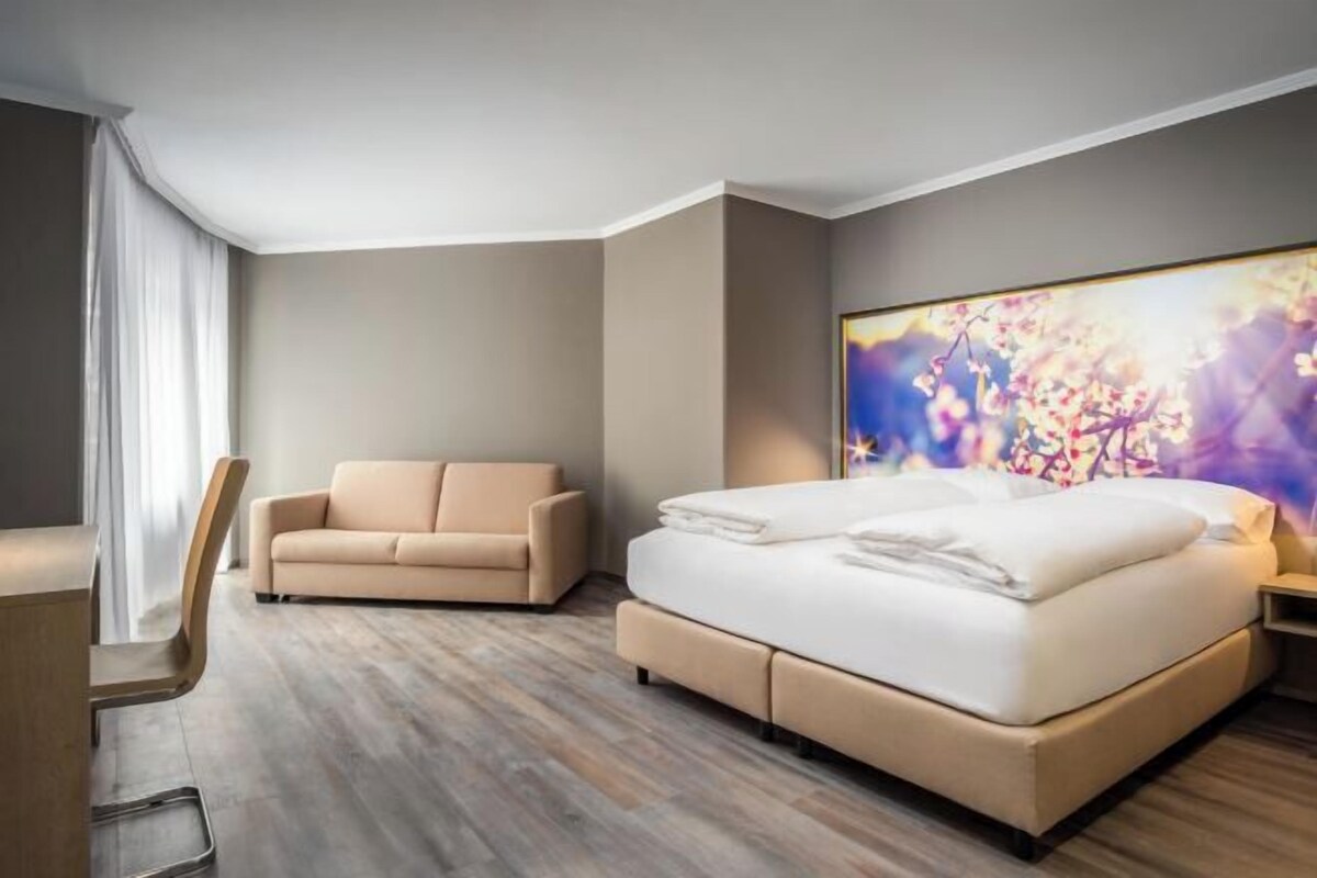 A modern hotel room with a bed, a sofa, and a large window.
