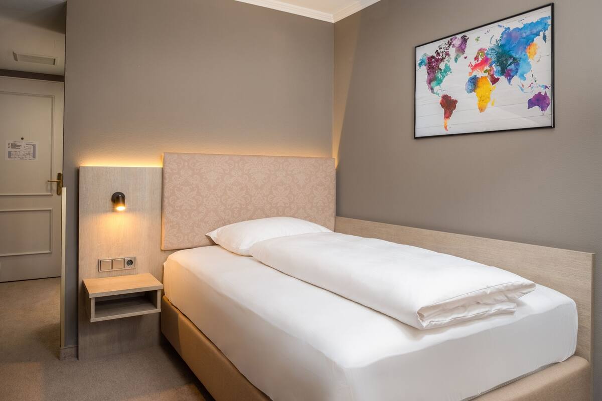 A neatly made bed with a headboard, a bedside table with a lamp, and a world map artwork on the wall.