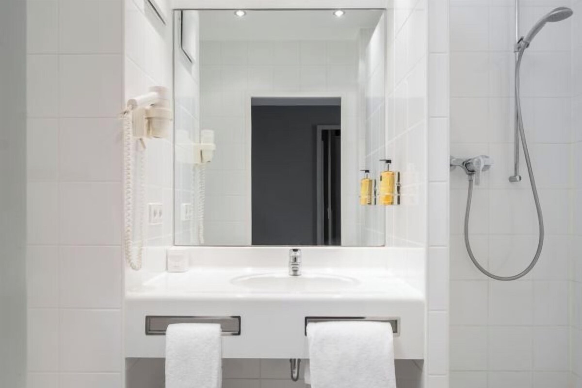 Un baño con lavamanos blanco, espejo y toallero.