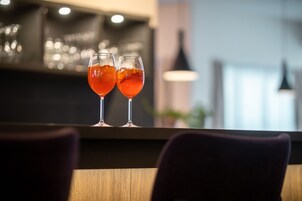 Two glasses of red beverage on a bar counter with a blurred background of a bar area.