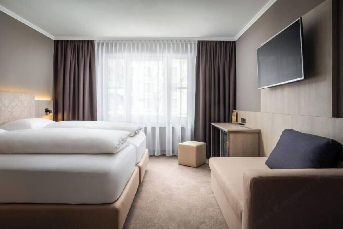 A hotel room with a bed, a sofa, a TV, and a small table.