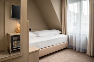 Quarto moderno com cama, mesa de cabeceira, televisão embutida e minibar.