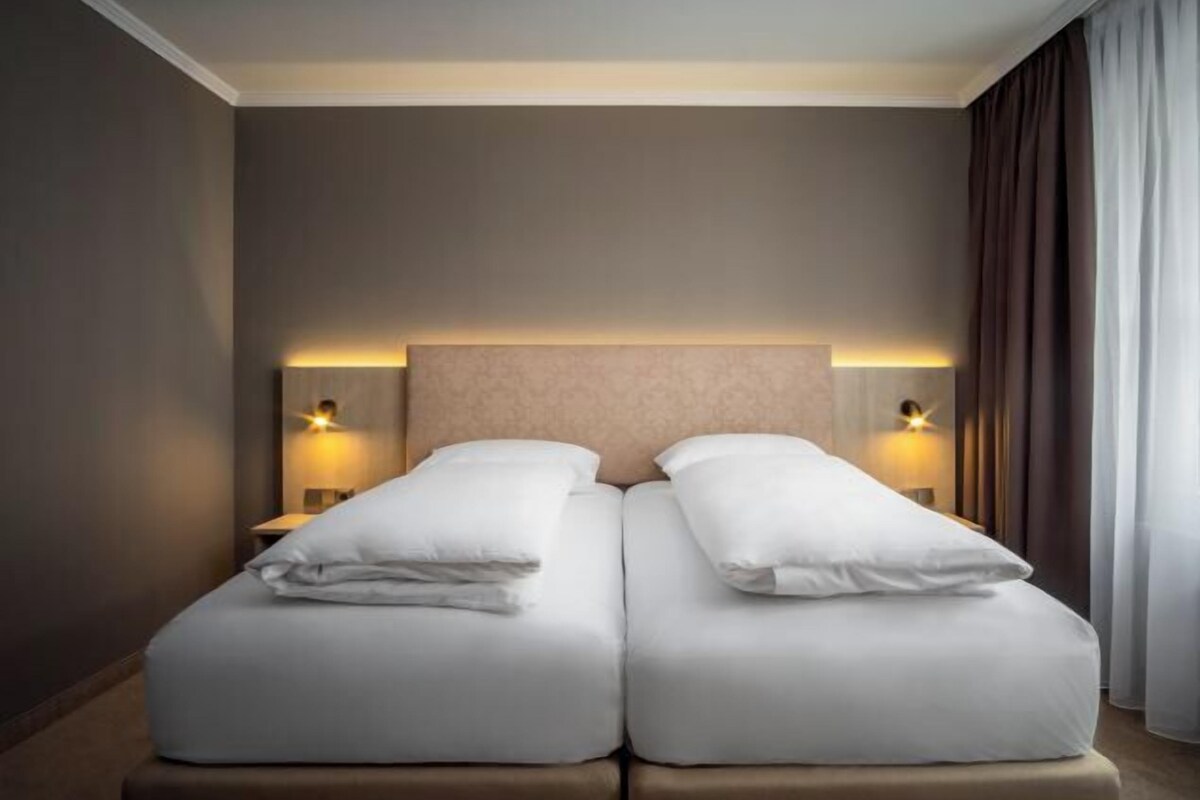 A double bed with white linens, two bedside lamps, and a neutral-toned headboard.