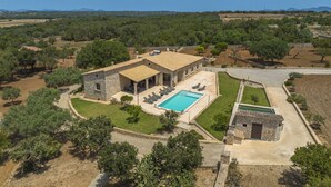 A stone villa with a swimming pool, surrounded by lush greenery and a clear view of the countryside.
