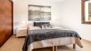 A bedroom with a bed, two bedside tables, a nightstand, a window, and a wall-mounted artwork.