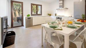 A modern kitchen with white cabinetry, a built-in dishwasher, and a dining area set for six with green plates and white chairs.