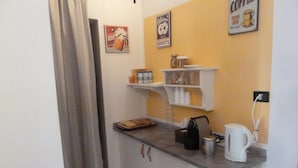 A small kitchenette with a coffee maker, a kettle, and a tray of pastries. There are shelves with jars and a poster on the wall. - Rabadan Bed and Breakfast (Turin)