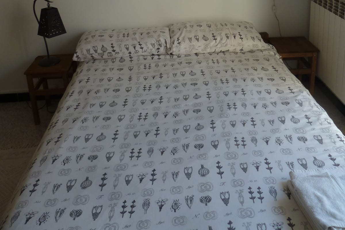 Un dormitorio con cama, mesita de noche, lámpara, un cuadro abstracto enmarcado y una estantería.