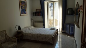 A bedroom with a bed, a chair, a bedside table, a radiator, a bookshelf, a wardrobe, and a window with curtains. - Rabadan Bed and Breakfast (Turin)