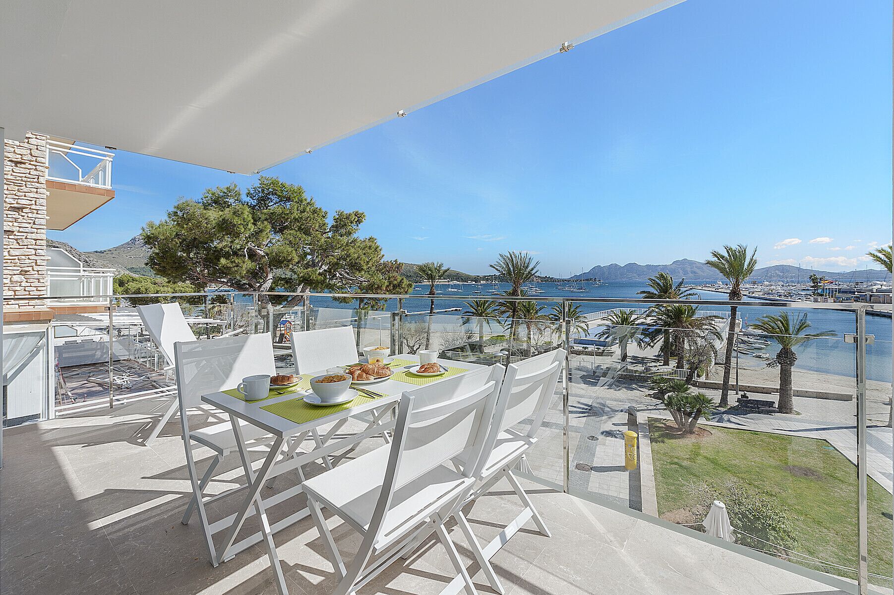 A balcony with a table set for breakfast, overlooking a marina with boats and a clear sky.