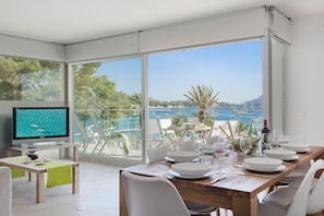 Un comedor moderno con vista al mar, un televisor y una mesa preparada para dos.