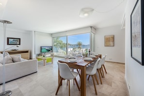 A modern living room with a dining area, large windows, and a TV.