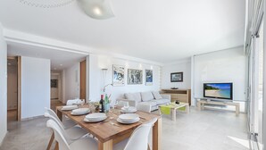 Ein modernes Wohnzimmer mit Essbereich, einer Couch, einem Fernseher und Kunstwerken an den Wänden.