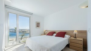 Ein Schlafzimmer mit einem Bett, zwei Nachttischen, einem Fenster mit Blick auf eine Marina und einer Tür.