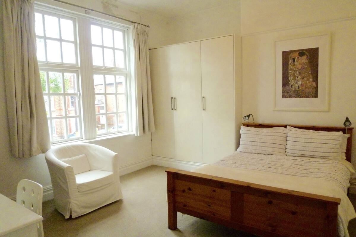 A bedroom with a bed, a chair, a wardrobe, and a window with curtains.