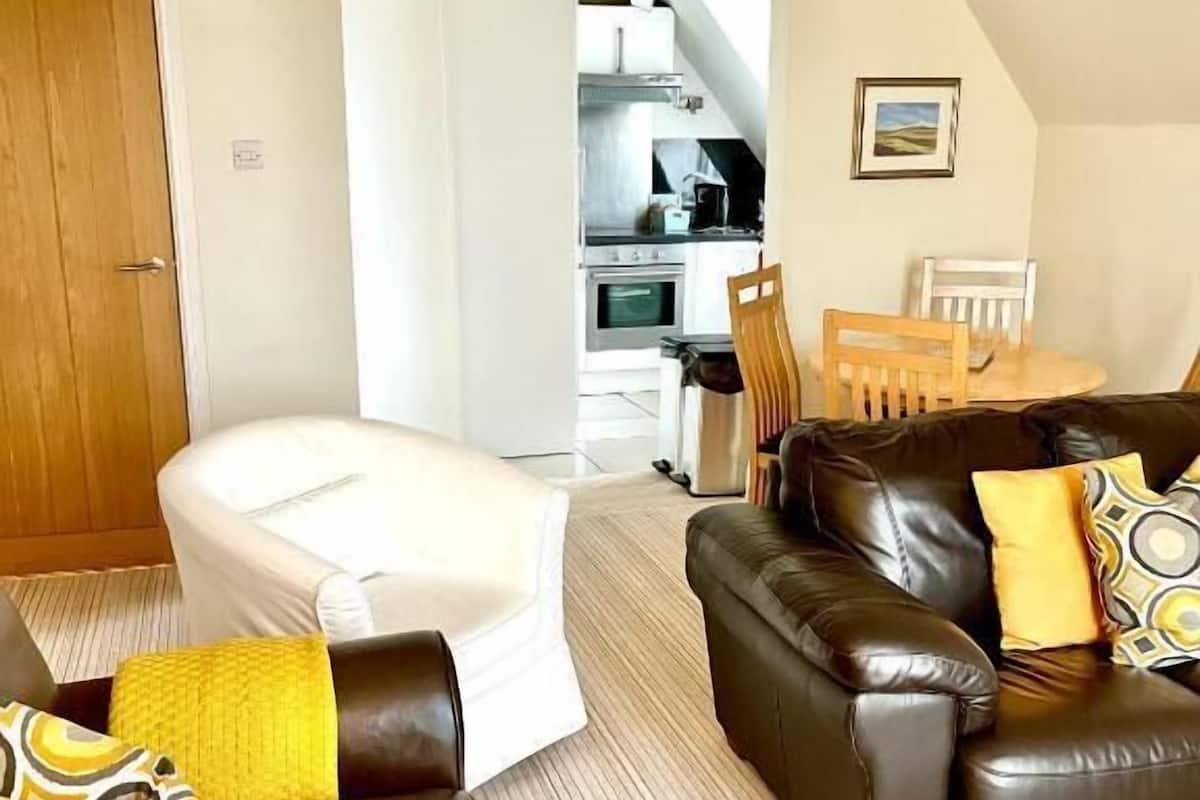 A modern living room with a sofa, a small table, and a bathtub. There is a kitchen in the background.