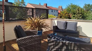 An outdoor patio with wicker furniture, a potted plant, and a view of neighboring houses. - Holland House (Wallasey)