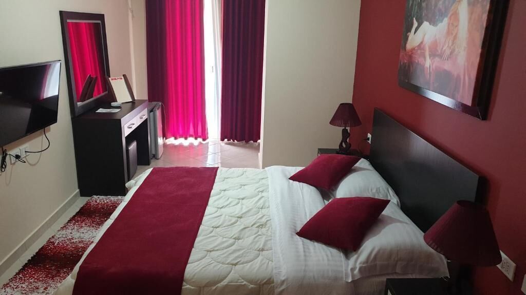 Habitación de hotel con cama, escritorio, televisión y ventana con cortinas.