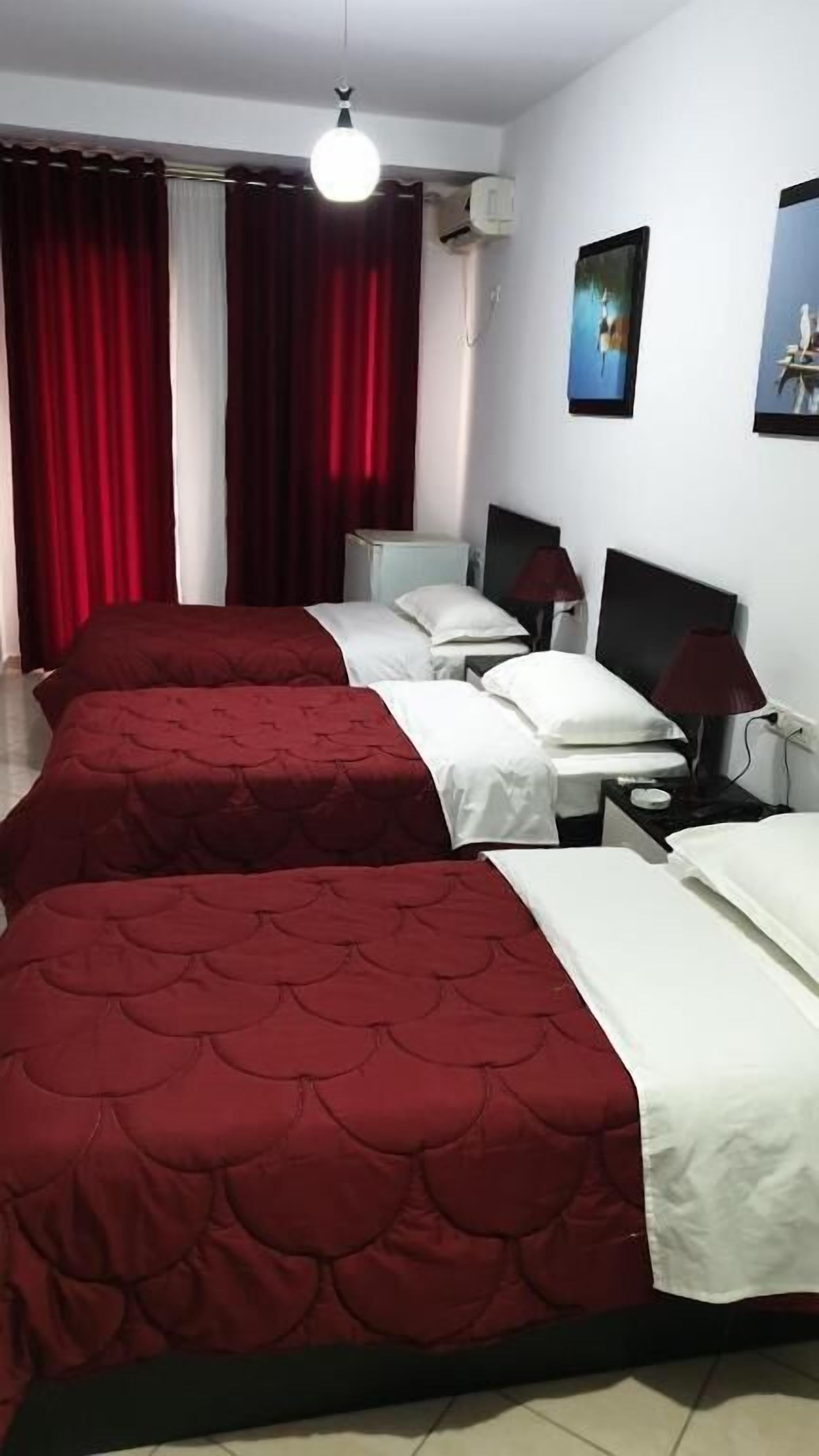 Habitación de hotel con dos camas, televisión, lámpara y ventana con cortinas.