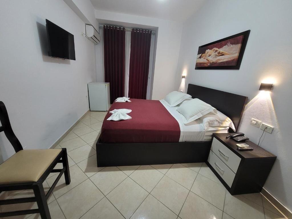 Ein Hotelzimmer mit einem Bett, einem Schreibtisch mit Telefon, einem Sessel, einem Fernseher und einem Bild an der Wand.