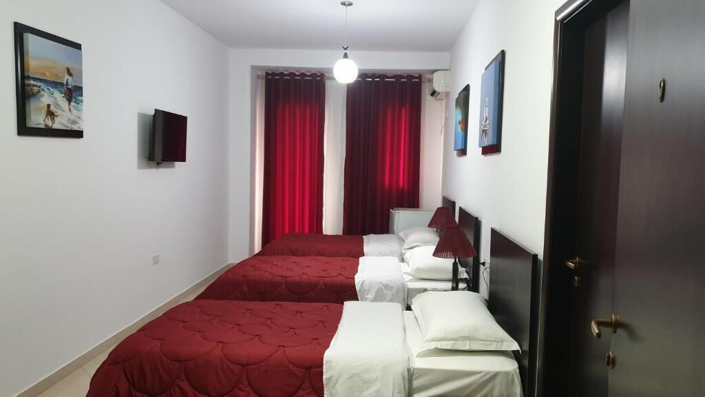 Ein Hotelzimmer mit zwei Betten, roten Vorhängen, einem Fernseher und einer Tür.