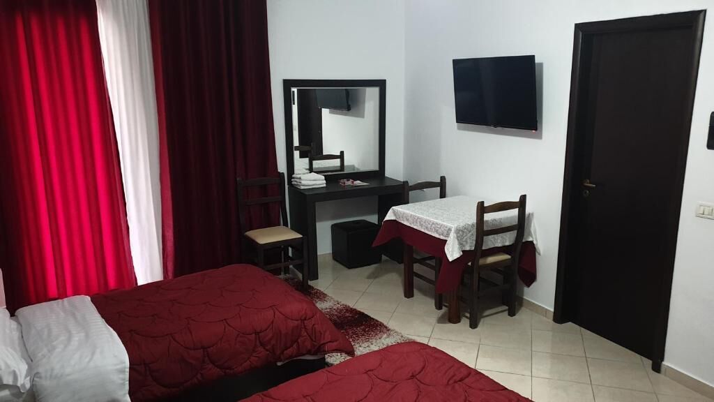 A bedroom with two beds, a desk with a chair, a mirror, a television, and a door.