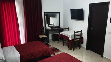 A bedroom with two beds, a desk with a chair, a mirror, a television, and a door.