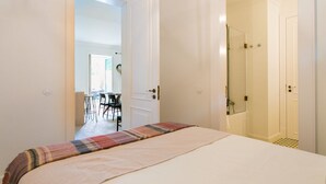 A hotel room with a bed, a shower, and a view of a dining area.