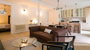 A modern living room with a brown sofa, a glass coffee table, and a dining area with a kitchen in the background.