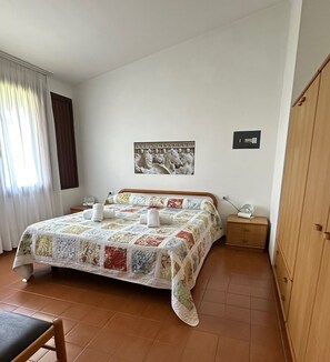 A bedroom with a bed, a nightstand, a wooden wardrobe, a framed picture on the wall, and a window with curtains. - Residence Barbara (Moniga del Garda)