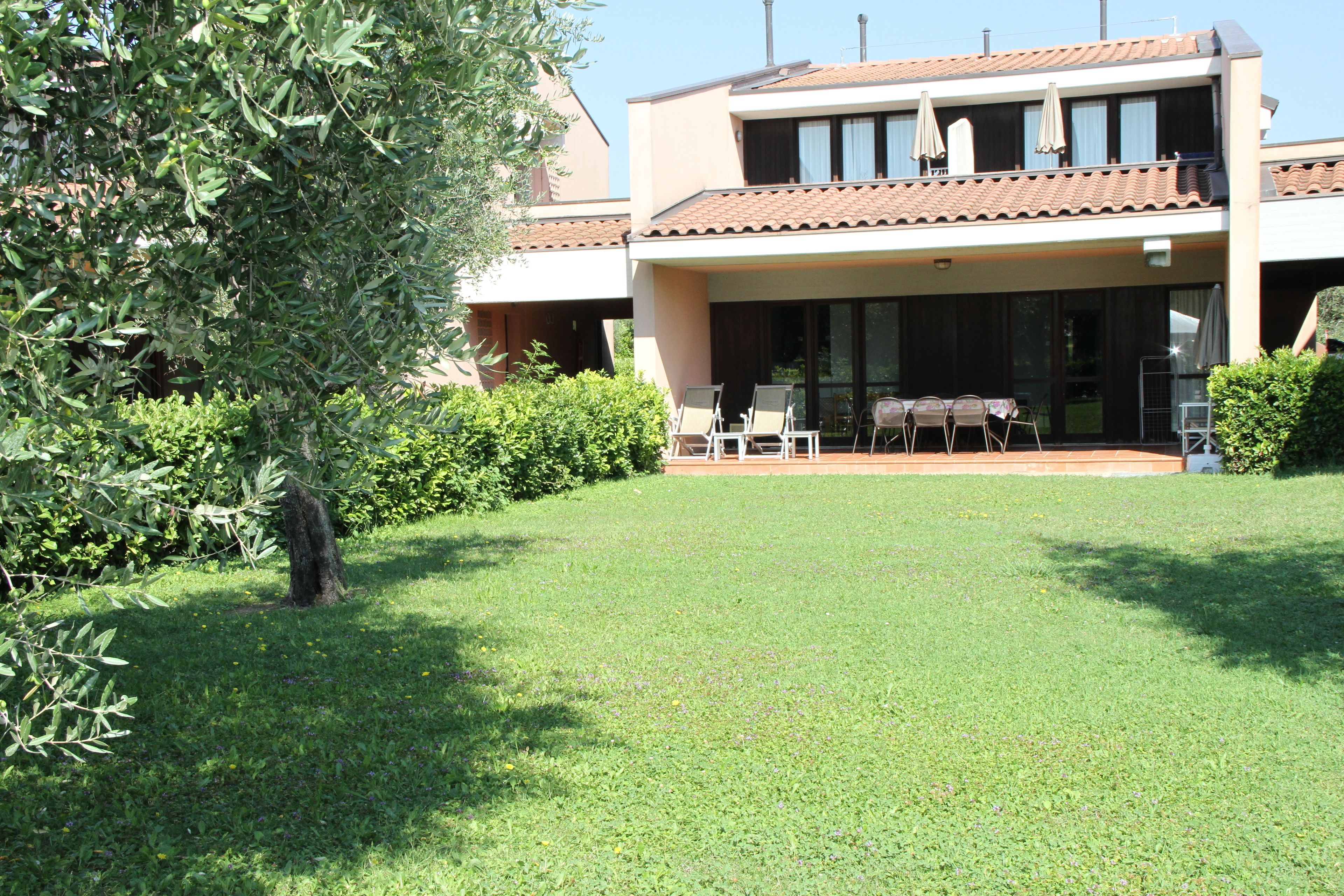 A two-story house with a covered patio area, a lawn, and a tree.