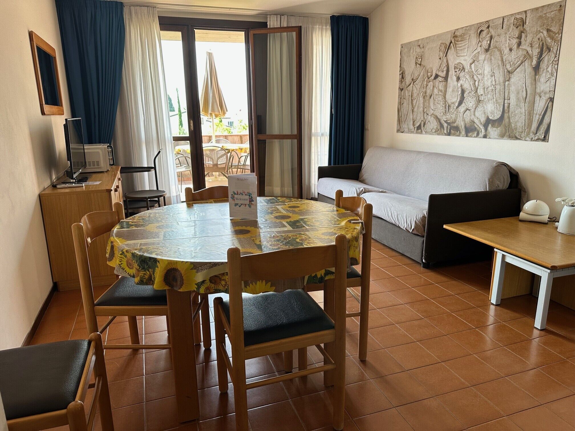 A room with a round table, chairs, a sofa, a small cabinet, and a painting on the wall.