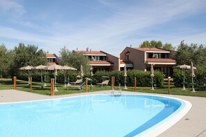 A swimming pool with lounge chairs and umbrellas, surrounded by buildings with red-tiled roofs. - Residence Barbara (Moniga del Garda)