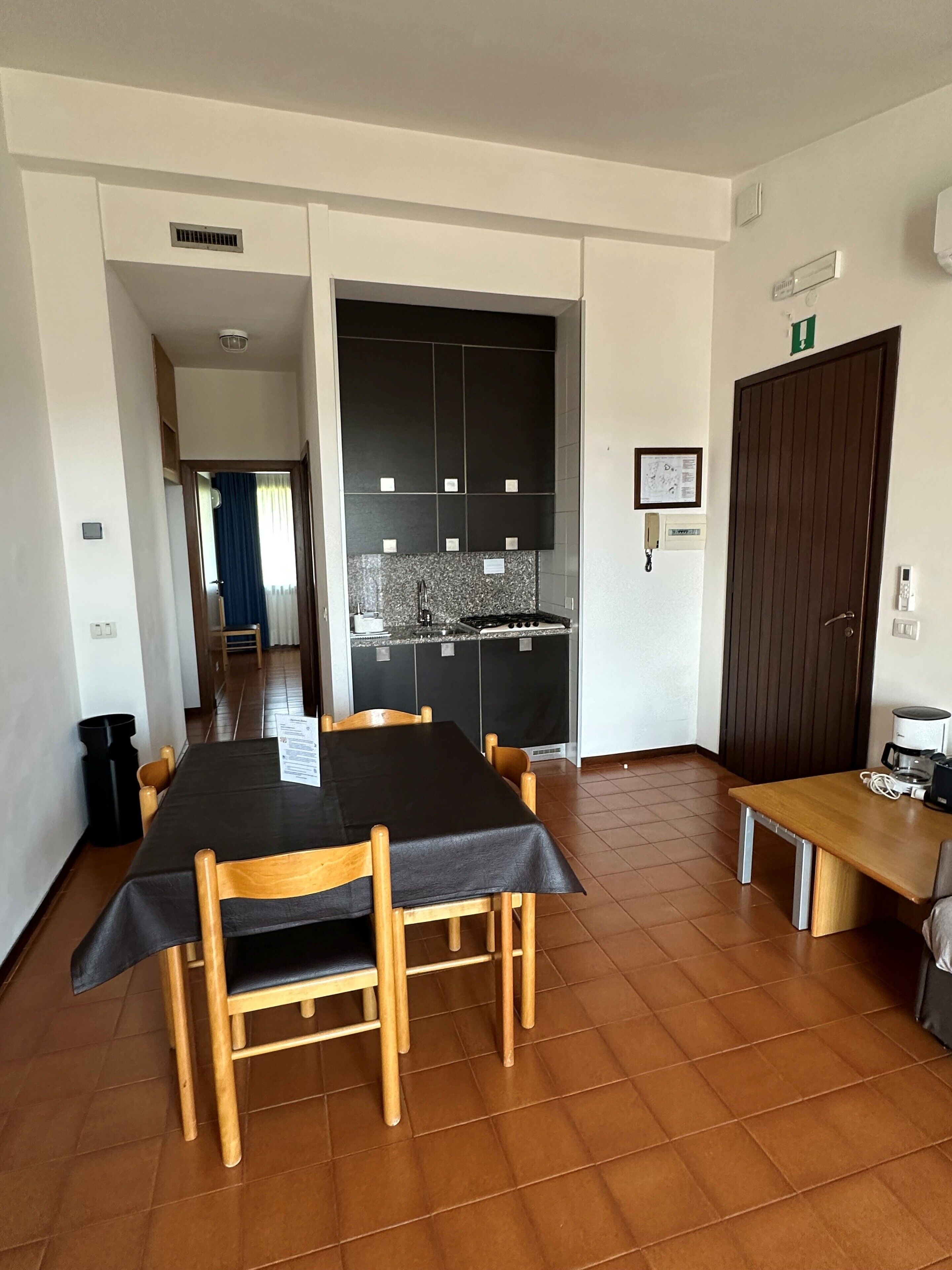 Een eetgedeelte met een tafel en stoelen, een keuken op de achtergrond, en een deur naar een andere kamer.