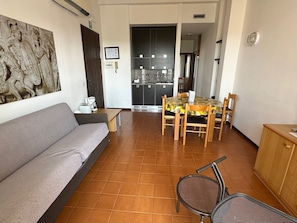 A living room with a sofa, a dining table with chairs, a kitchen area, and a door leading to another room. - Residence Barbara (Moniga del Garda)