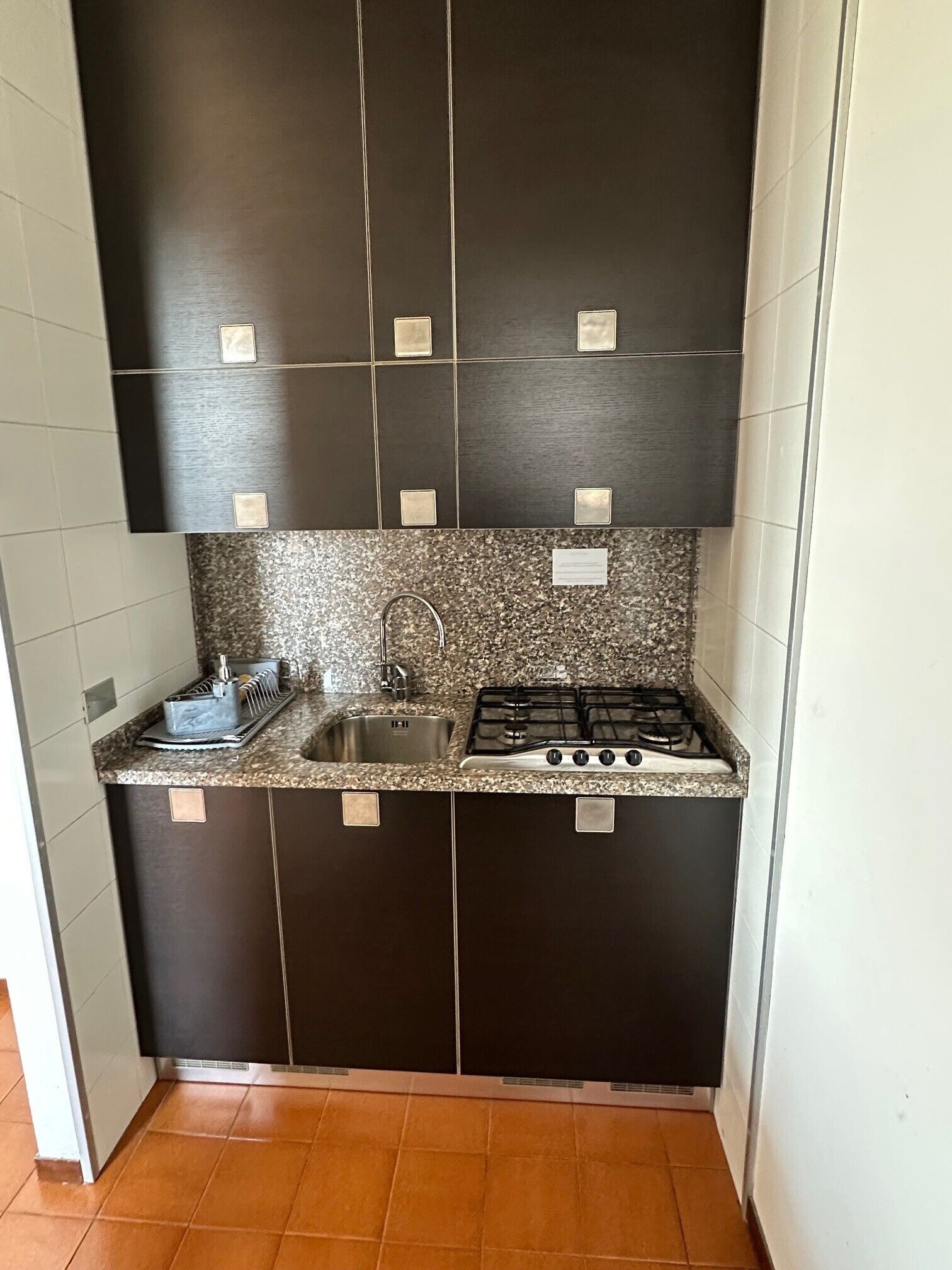 Una cucina compatta con mobili scuri, un piano di lavoro in granito, un lavello in acciaio inossidabile e un piano cottura a gas.