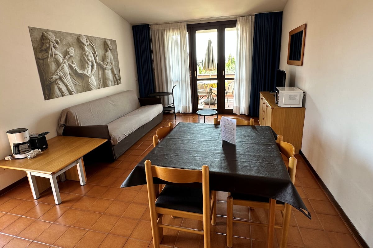 A dining area with a table, chairs, a sofa, a coffee machine, and a painting on the wall.