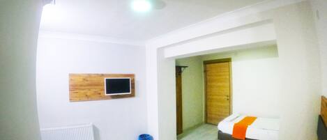 Habitación de hotel con cama, mesita de noche, espejo, ventana y televisor de pared.
