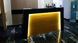 A reception desk with a wooden panel and a black frame, a white wall with a geometric pattern, and a marble floor. - Ankara Otel Evren (Ankara)
