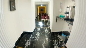 A hallway with a black marble floor, a wooden cabinet, and a coffee machine on the right. - Ankara Otel Evren (Ankara)