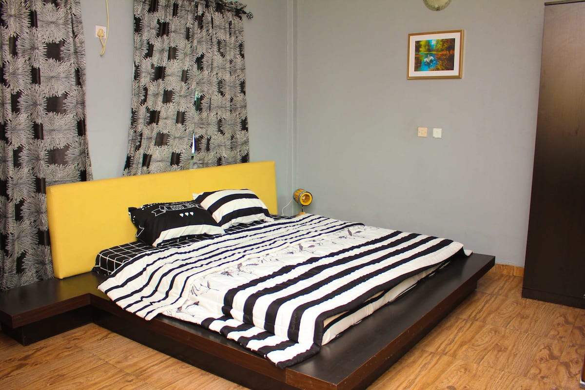 A bedroom with a bed, curtains, a painting, and a wooden floor.