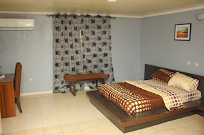A bedroom with a bed, a bench, a desk, and an air conditioner. - InnTown Studios (Lekki)