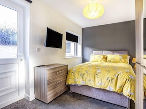 Un dormitorio con cama, cómoda, televisor y ventana.